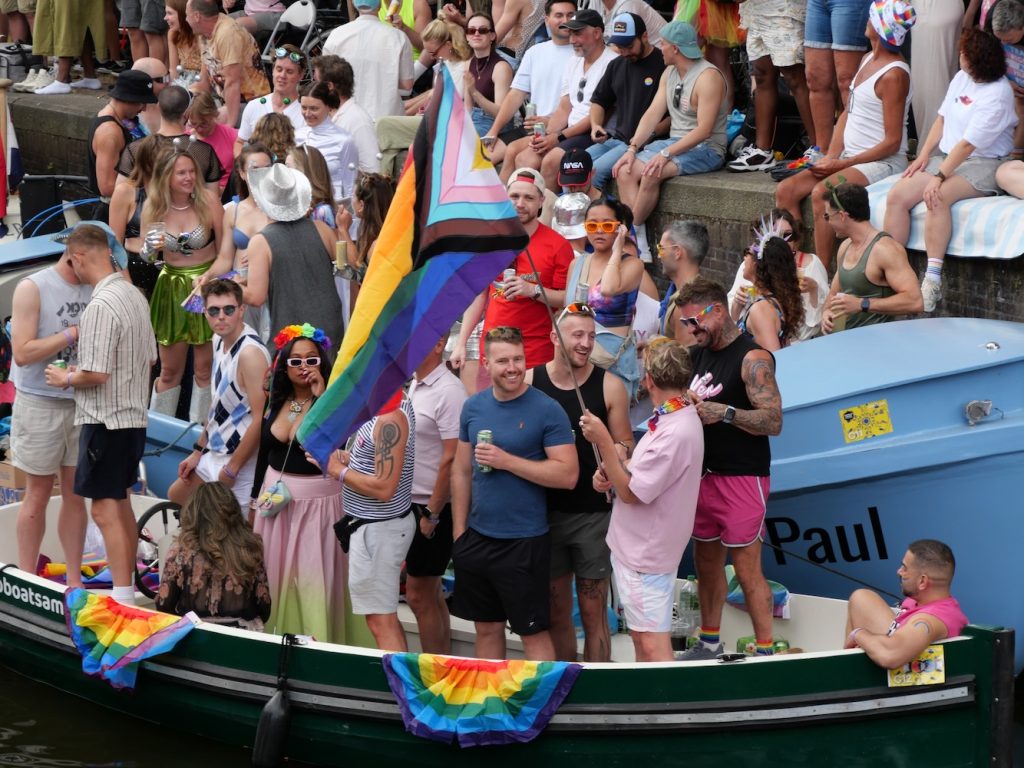 Spectators on a boat watch and wave a rainbow flag during Amsterdam World Pride 2026 Canal Parade.