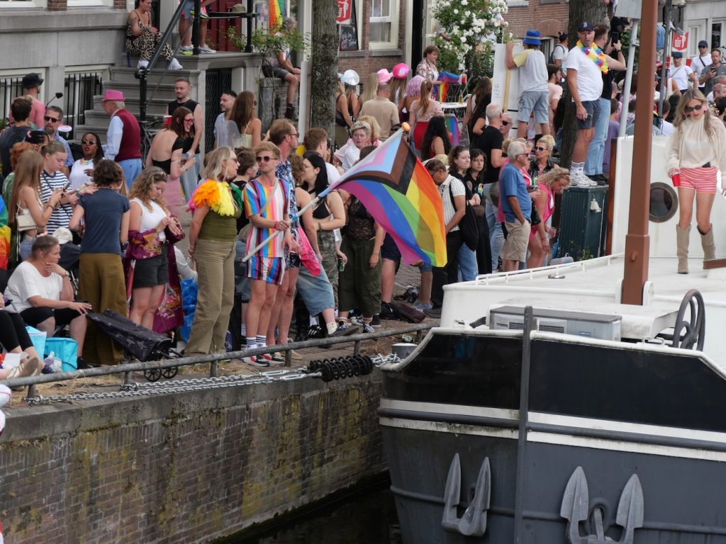 Spectators watch and wave a rainbow flag during Amsterdam World Pride 2026 Canal Parade.