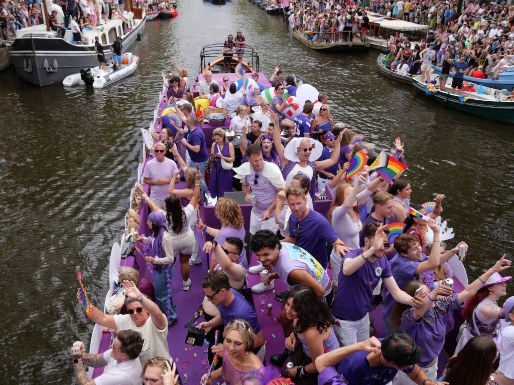 Volunteers on a float all dressed in shades of purple & lilac for Amsterdam World Pride 2026 Canal Parade.