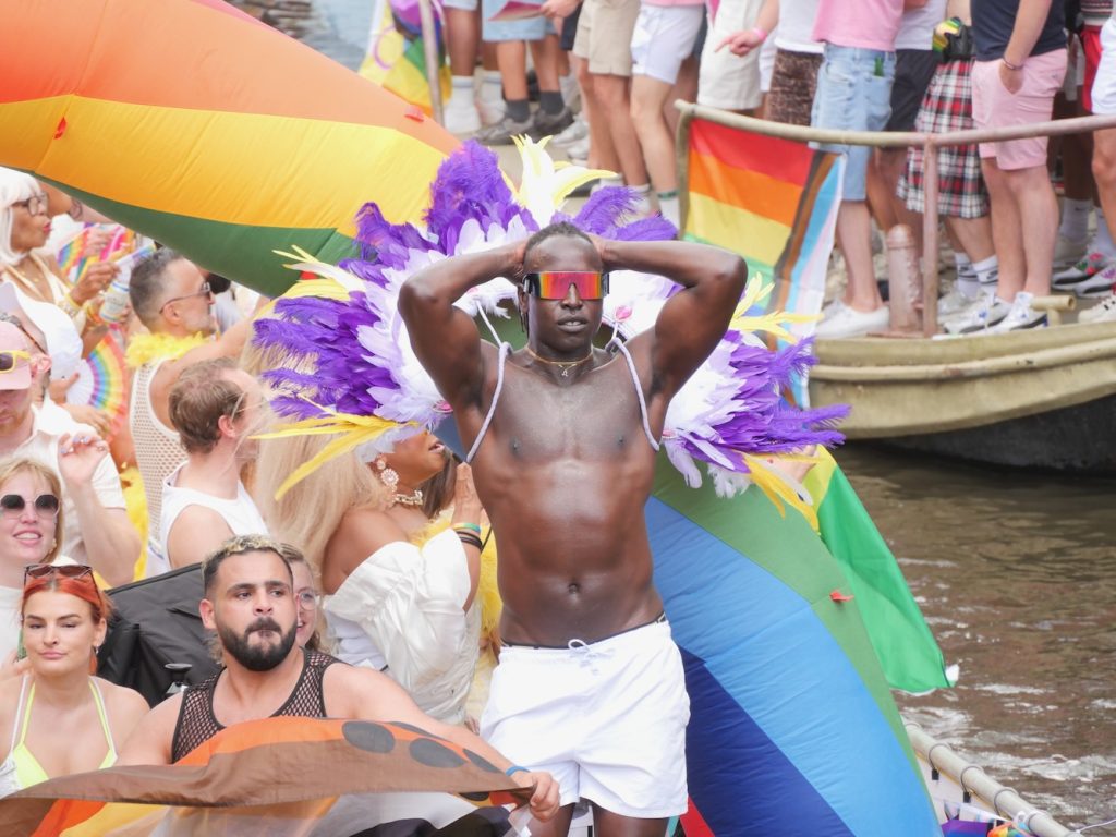 A man dances with white and purple feathers during Amsterdam World Pride 2026 Canal Parade.