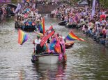 A small boat with multiple rainbow flags and one Amsterdam XXX flag during the Amsterdam World Pride 2026 Canal Parade.